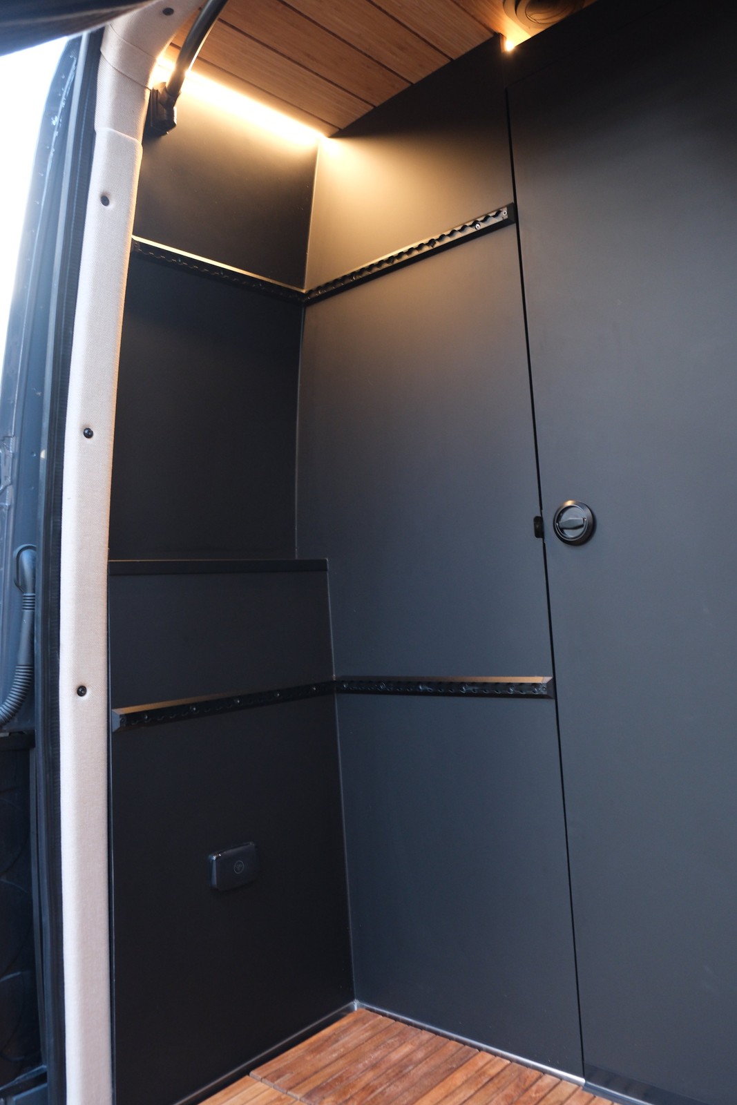 The Den dark rear shower walls and wood trim, viewed with the rear doors open.